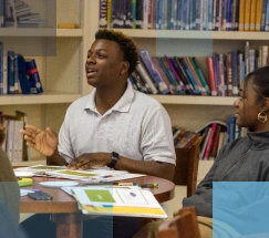 Estudiante de secundaria afroamericano y estudiante de secundaria afroamericana sentados en una mesa en la biblioteca