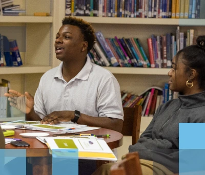 Estudiante de secundaria afroamericano y estudiante de secundaria afroamericana sentados en una mesa en la biblioteca