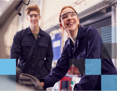 A smiling male and a smiling female high school student working under the hood of an automobile in an auto shop setting